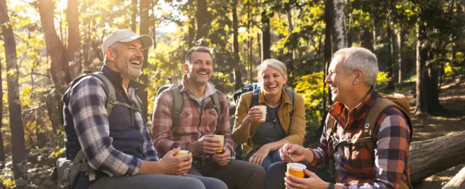 Zwei Paare 50+ beim Wandern, Pause auf Baumstamm mit Brotzeit, lachend und voller Energie – Symbol für Slow Aging und TCM