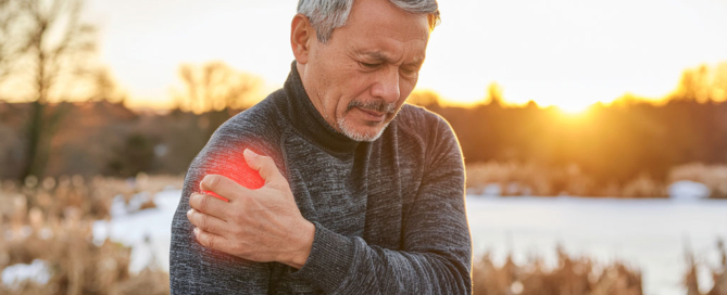 Mann hält sich schmerzende Schulter im Winterlicht – Symbol für Gelenkschmerzen und Linderung durch TCM